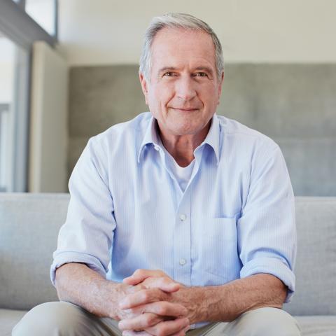 Man in his fifties seated on a sofa, smiling and looking confident