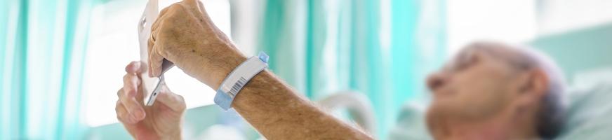 Patient hospitalisé, allongé dans son lit, regarde son smartphone