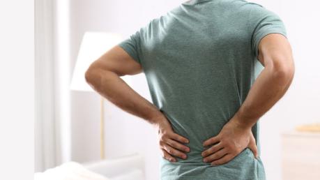Homme debout, se tenant le bas du dos avec ses deux mains - douleur aux lombaires
